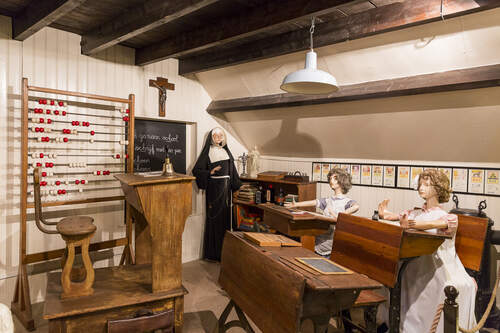 Klaslokaaltje met poppen van twee leerlingen en een non in Museum Oud Oosterhout