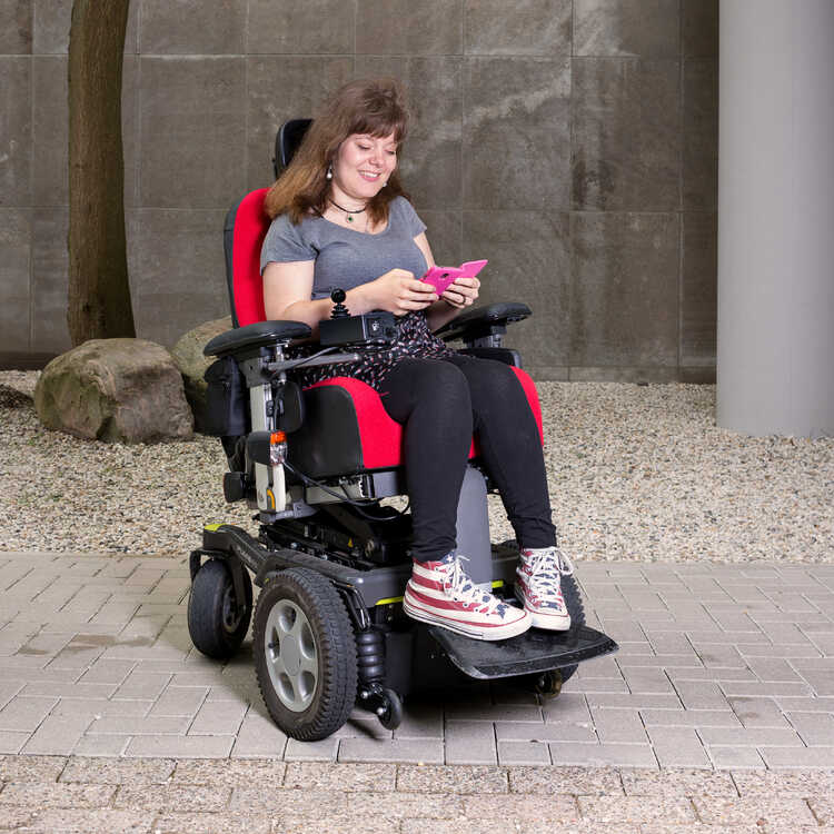 Amber Bindels, zit in een rolstoel en kijkt op haar telefoon. Fotograaf Tessa Spaaij. Eigenaar Stichting Zet.
