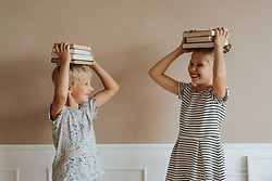 Twee lachende kinderen staan en houden een stapel boeken op hun hoofd Bron Pexels Fotograaf Olia Danilevich