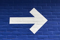 Witte pijl geschilderd op een blauwe muur Foto Rick Fewings via Unsplash